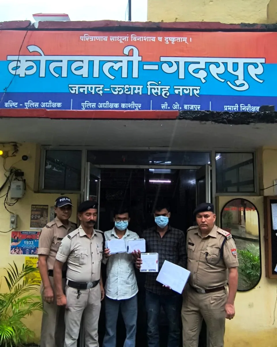 कोतवाली गदरपुर के बाहर पुलिसकर्मियों के साथ मास्क पहने दो आरोपी, हाथ में बरामद दस्तावेज